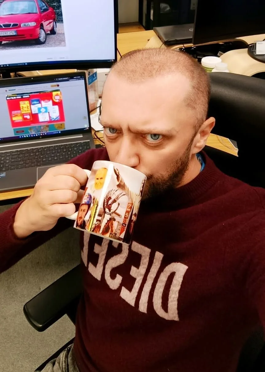 Jakub Kodymowski przy komputerach, z kubkiem w dłoni
